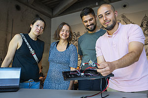 Eine Professorin und drei Studierende, einer davon hält eine Computerplatine in die Kamera