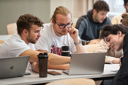 Drei Studierende setzen an einem Computer ein KI-Projekt um
